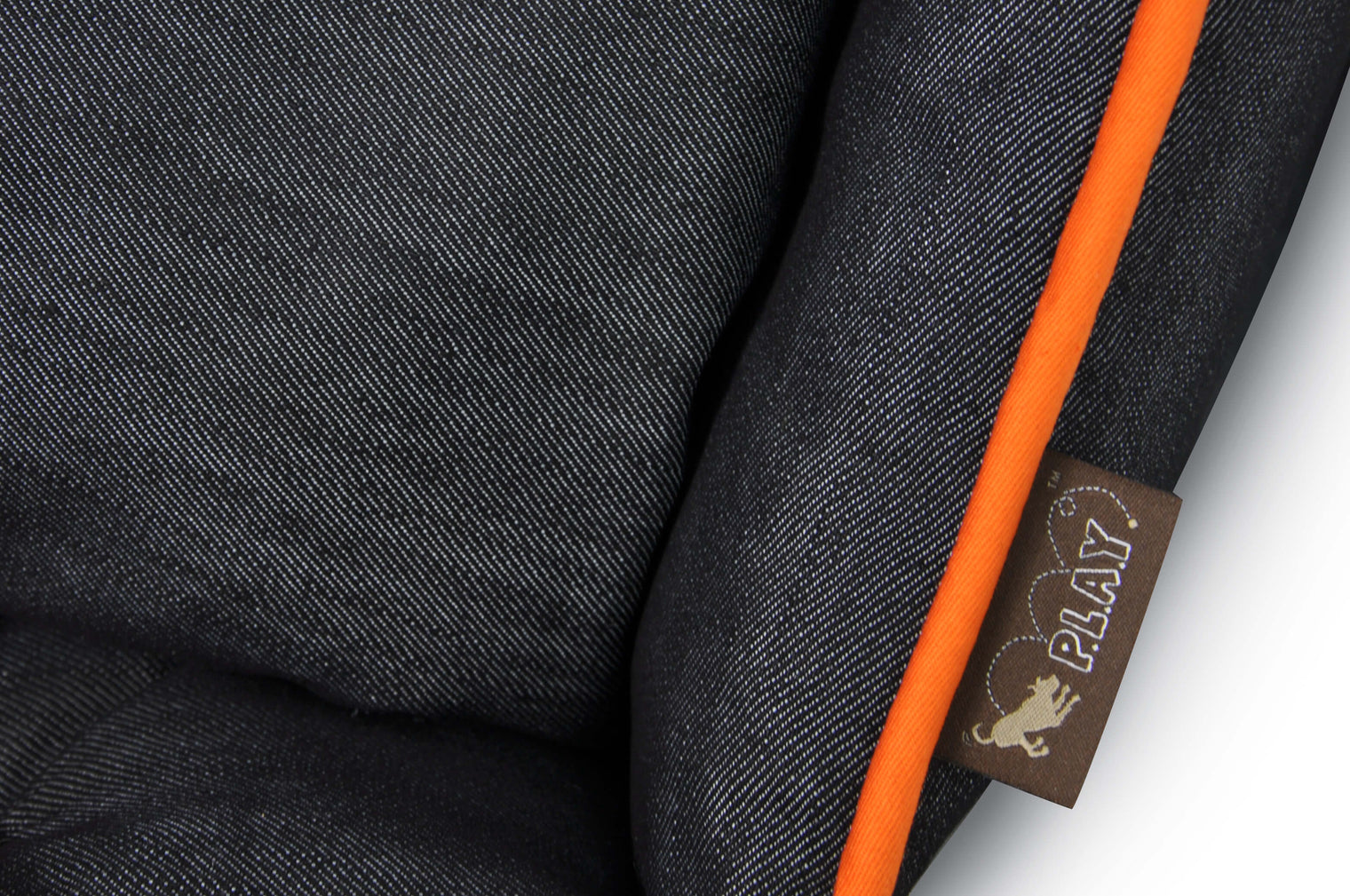 Close-up of P.L.A.Y. Denim Lounge Bed with orange piping and brand tag.