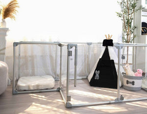 Clear dog pen with teepee bed, basket of toys and bed.