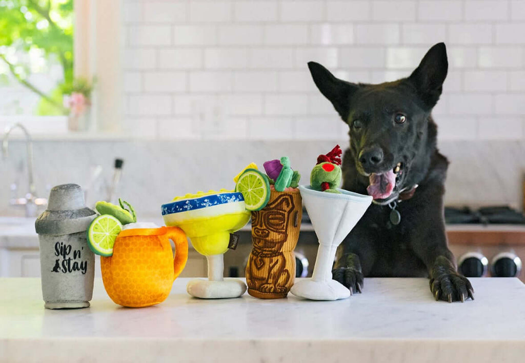 Dog with P.L.A.Y. Barktender Toy Set, featuring cocktail-inspired plush toys on a kitchen counter.