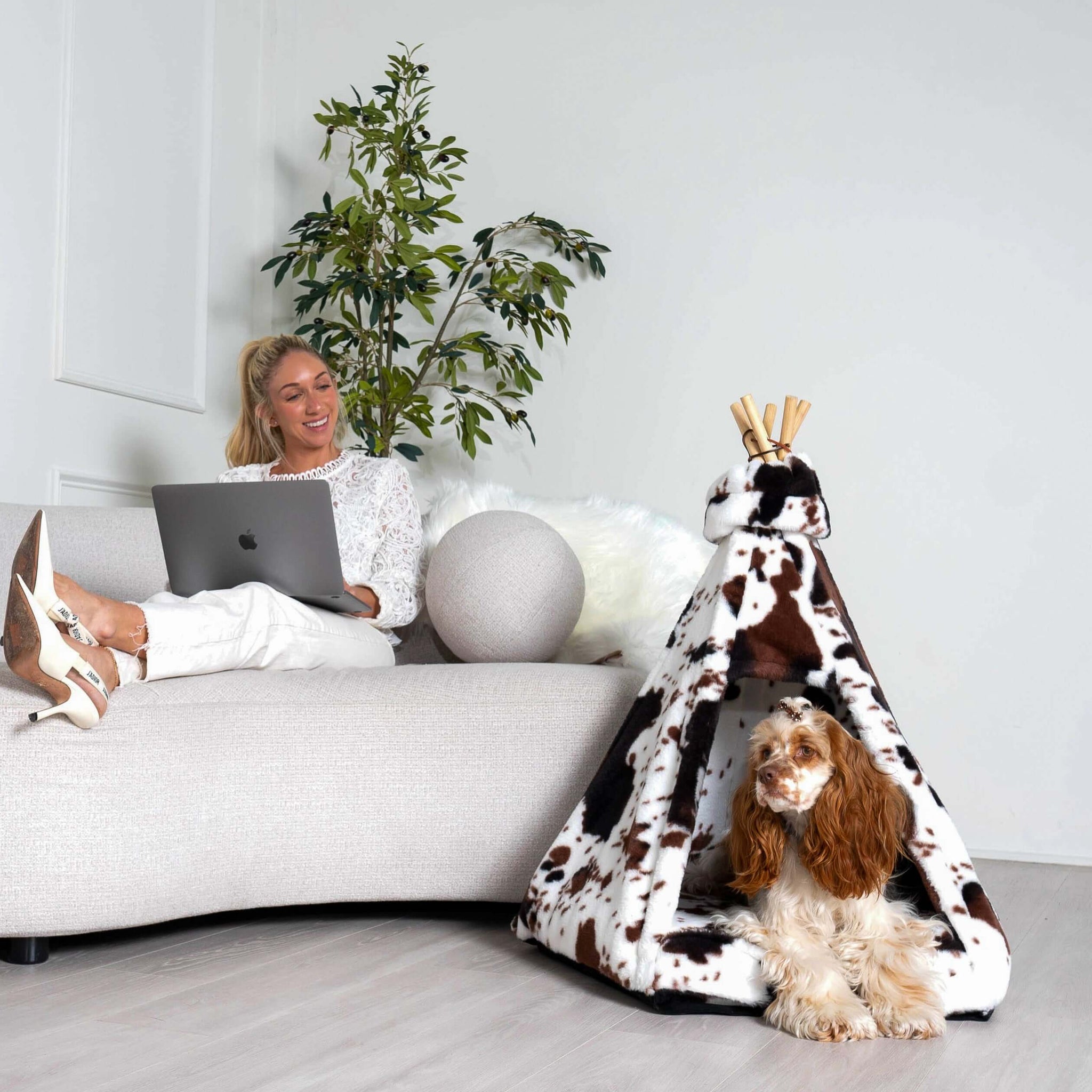 Woman sitting next to luxurious pet bed teepee with dog resting inside