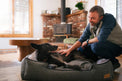 Man petting a happy dog on a P.L.A.Y. Houndstooth Lounge Bed in a cozy living room.