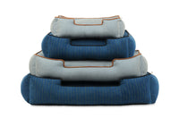 Stack of P.L.A.Y. Manhattan Lounge Beds in bolster style showcasing assorted sizes and blue tones for ultimate pet comfort.