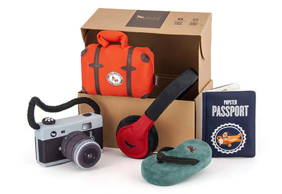 P.L.A.Y. Globetrotter Toy Set with plush suitcase, camera, sandal, earmuffs, and Pupster Passport for playful pups.