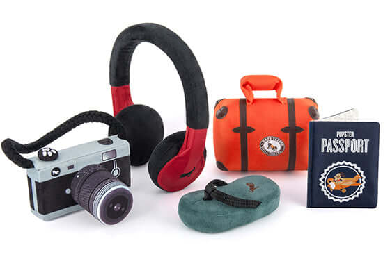 "P.L.A.Y. Globetrotter Toy Set featuring plush camera, travel bag, headphones, shoe toy, and Pupster Passport for dogs' adventure play."