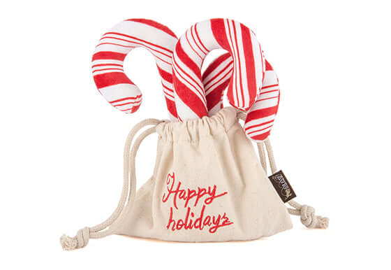 P.L.A.Y. holiday dog toy set with plush candy canes in a festive bag with "Happy Holidays" text.