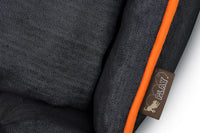 Close-up of P.L.A.Y. Denim Lounge Bed with orange piping and brand tag.