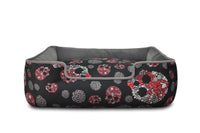 Skulls & Roses dog bed with raised sides and reversible cushion, featuring skull motif, roses, and baby's breath for stylish pet comfort.